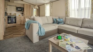 En moderne stue med sofa, sofabord med blade, samt et køkkenområde med træskabe og en mikrobølgeovn.