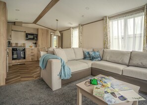 Een moderne woonkamer met een bank, een salontafel met tijdschriften, en een keuken met houten kastjes en een magnetron.