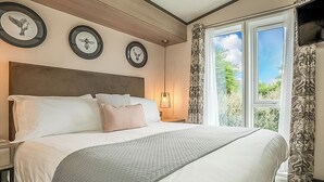 A bedroom with a large bed, a nightstand, a wall-mounted lamp, and a window with curtains. - 1 bedroom accommodation in Mawgan Porth, Nr Newquay (Mawgan Porth, Nr Newquay)