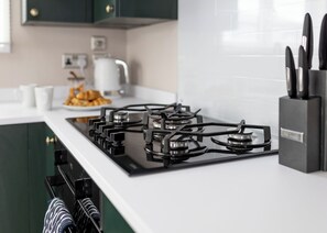Eine moderne Küche mit Gasherd, weißen Arbeitsplatten und grünen Schränken.