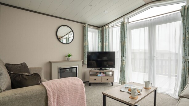 A living room with a sofa, a coffee table, a TV, a small cabinet, and a balcony with curtains. - 1 bedroom accommodation in Mawgan Porth, Nr Newquay (Mawgan Porth, Nr Newquay)