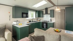 A compact kitchen with a microwave, stove, and sink, a dining area with a table and chairs, and a large window providing natural light. - 1 bedroom accommodation in Mawgan Porth, Nr Newquay (Mawgan Porth, Nr Newquay)