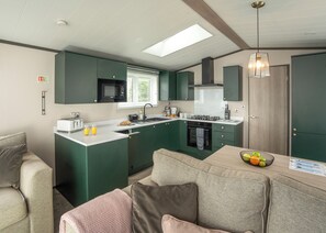 A compact kitchen with a microwave, stove, and sink, a dining area with a table and chairs, and a large window providing natural light. - 1 bedroom accommodation in Mawgan Porth, Nr Newquay (Mawgan Porth, Nr Newquay)