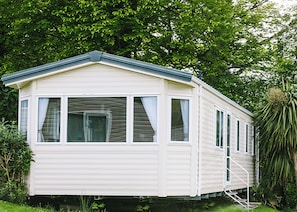 A single-story mobile home with a gabled roof, large windows, and a small porch area.
