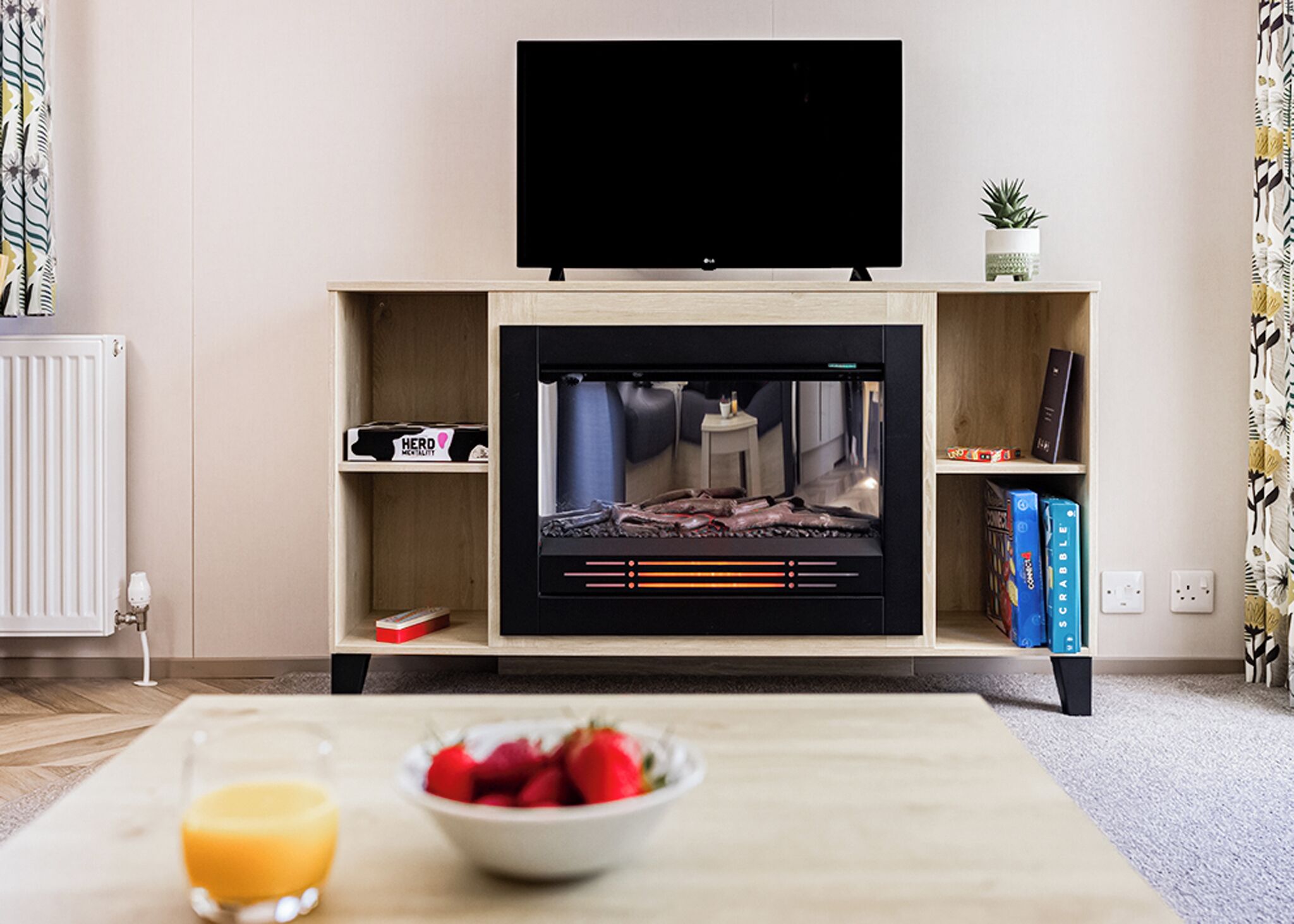 Una sala de estar con un televisor de pantalla plana, una chimenea, una mesa de centro con un frutero y una estantería.