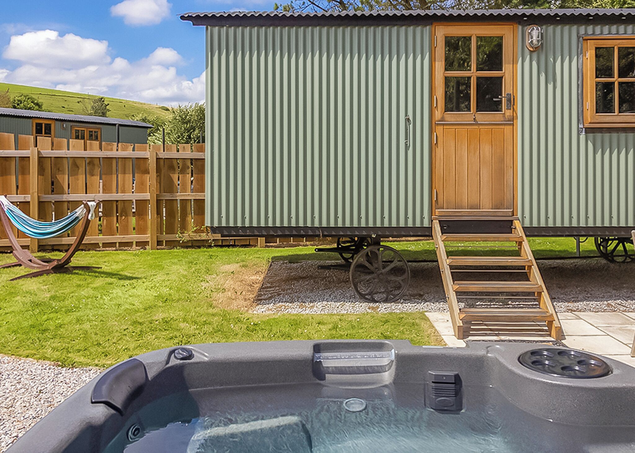 A hot tub with a wooden ladder, a hammock, and a metal building with a door and windows.