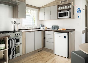 A compact kitchen with a stove, oven, microwave, and a small refrigerator. - Standard 2 Bed (Pet) (Mawgan Porth, Nr Newquay)