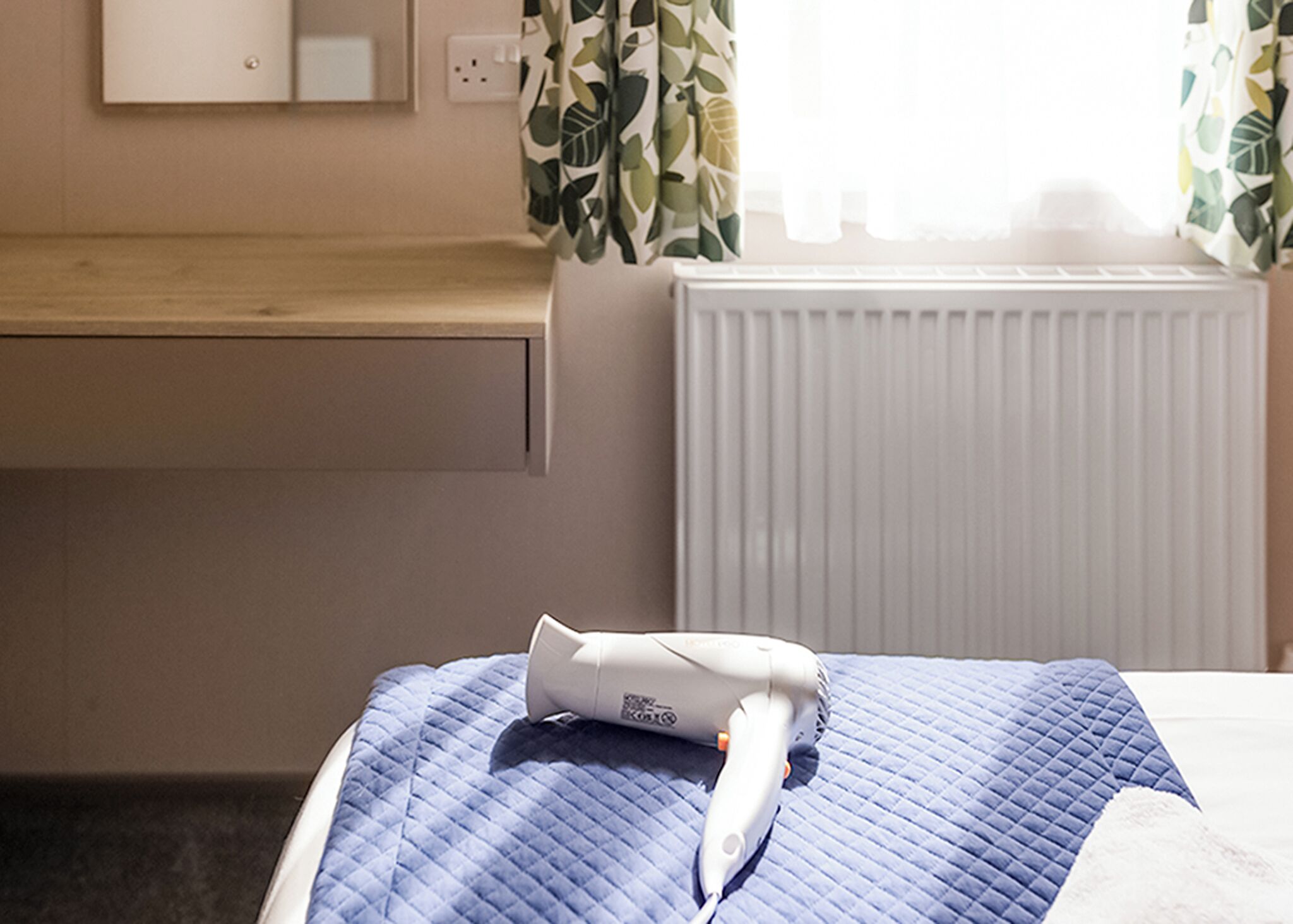 Een hotelkamer met een bed, een haardroger, een raam met gordijnen, een radiator en een houten toonbank.