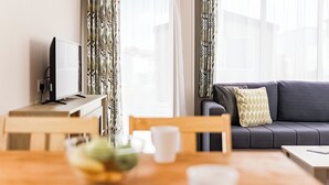 A modern living room with a sofa, a dining table with chairs, a TV, and a window with curtains. - Standard 2 Bed (Pet) (Mawgan Porth, Nr Newquay)
