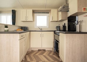 A compact kitchen with a herringbone floor pattern, a window, and basic appliances. - The Superior 2 Bedroom is a comfortable and spacious sleeps 6 caravan. (Mawgan Porth, Nr Newquay)