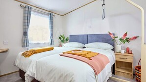 Een slaapkamer met een bed, nachtkastjes, een raam met gordijnen, een plant en een douche.