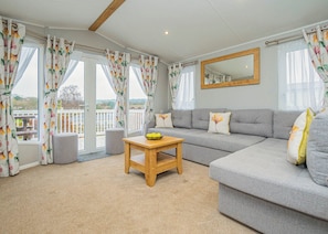 A living room with a grey sofa, a wooden coffee table, and a balcony with curtains. - 3 bedroom accommodation in Dawlish (Dawlish)