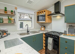 A modern kitchen with a stove, sink, and wooden cabinets. - 3 bedroom accommodation in Dawlish (Dawlish)