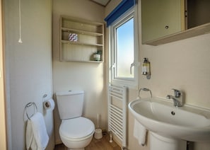 A compact bathroom with a toilet, a sink, a window, and a shelf with a plant. - The Superior 3 Bedroom is a comfortable and spacious sleeps 8 caravan. (Mawgan Porth, Nr Newquay)