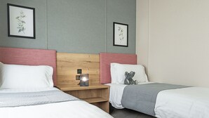 A hotel room with two beds, a nightstand with a lamp, and framed botanical prints on the wall.