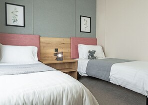 A hotel room with two beds, a nightstand with a lamp, and framed botanical prints on the wall.