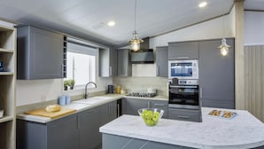 A modern kitchen with grey cabinets, a marble countertop, a built-in oven, and a central island with a bowl of apples.
