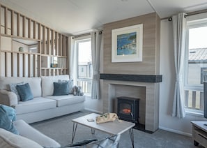 A living room with a sofa, a fireplace, a table, and a view of the outside.