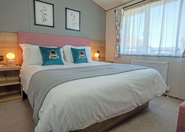 A neatly made bed with a headboard, two bedside lamps, and a window with sheer curtains.