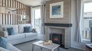 A living room with a sofa, a fireplace, a table, and a view of the outside.