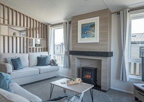A living room with a sofa, a fireplace, a table, and a view of the outside.