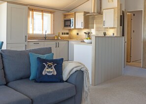 Cocina moderna con microondas, pileta y muebles de madera. Sofá gris con un cojín azul y diseño de abeja.