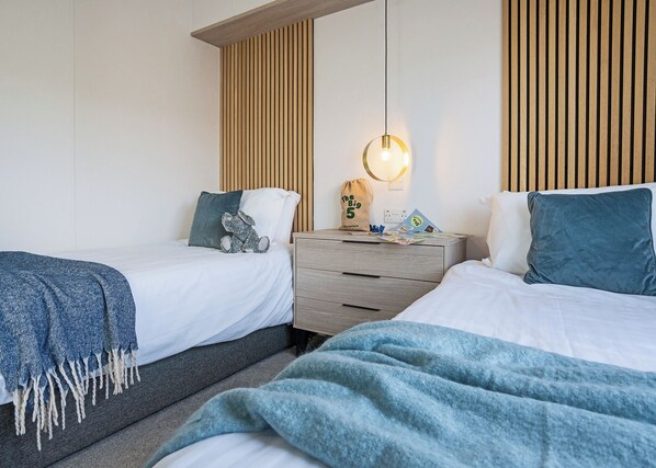 A hotel room with two beds, a wooden headboard, a nightstand with a lamp, and a plush toy on one bed.
