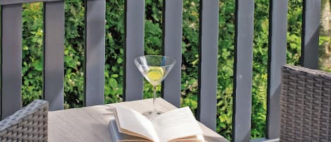 A wooden table with an open book and a martini glass with a lemon slice on a balcony.