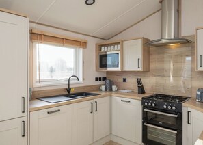 A modern kitchen with a gas stove, oven, microwave, and a window with blinds.