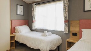 Un lit simple avec une literie blanche, une tête de lit en bois, une table de chevet, une fenêtre avec des rideaux et un tableau encadré au mur.