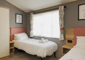 Ein Einzelbett mit weißer Bettwäsche, ein Holzkopfstück, ein Nachttisch, ein Fenster mit Vorhängen und ein gerahmtes Bild an der Wand.