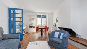 En stue med sofa, sofabord, en blå dør, et spiseområde med bord og stole, samt en pejs.