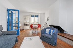 Ett vardagsrum med en soffa, ett soffbord, en matplats med bord och stolar samt en öppen spis.