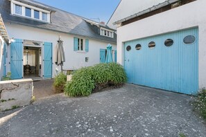 A courtyard with a blue garage door, a white building with blue shutters, and a green bush.