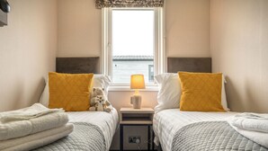 Ein Doppelzimmer mit zwei Betten, jedes mit einem gelben Kissen, einem Nachttisch mit Lampe und Meerblick durch ein Fenster.