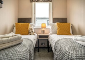 A twin room with two beds, each with a yellow pillow, a bedside table with a lamp, and a view of the sea through a window. - 1 bedroom accommodation in Padstow (Padstow)