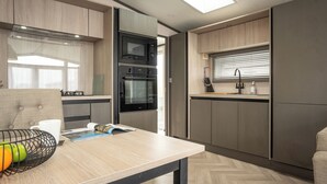 Eine moderne Küche mit eingebauten Geräten, eine Essecke mit Tisch und ein Fenster mit Jalousien.
