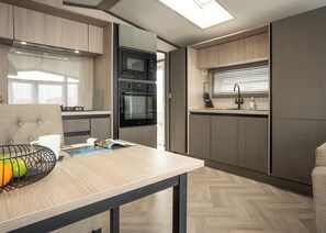 A modern kitchen with built-in appliances, a dining area with a table, and a window with blinds. - 1 bedroom accommodation in Padstow (Padstow)