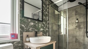 Ein Badezimmer mit einem weißen Waschbecken, einem Spiegel, einem Toilettenpapierhalter und einer Dusche mit Glastür.