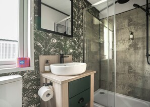 A bathroom with a white sink, a mirror, a toilet paper holder, and a shower with a glass door. - 1 bedroom accommodation in Padstow (Padstow)