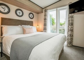 A bedroom with a bed, bedside tables, a wall-mounted TV, and framed pictures. - 1 bedroom accommodation in Padstow (Padstow)