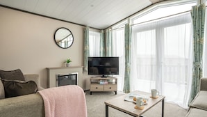Un salon comprenant un canapé, une table basse, un téléviseur, une cheminée et un balcon avec des rideaux.