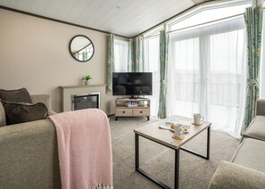 Ein Wohnzimmer mit Sofa, Couchtisch, Fernseher, Kamin und einem Balkon mit Vorhängen.