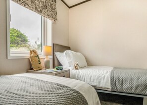 A hotel room with two beds, a window with a view of greenery, a lamp, a bag, and a small toy on the nightstand. - 1 bedroom accommodation in Padstow (Padstow)