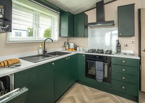 Eine kleine Küche mit grünen Schränken, einem Gasherd, einem eingebauten Backofen und einem Fenster mit Jalousien.