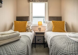 A twin room with two beds, a nightstand, a lamp, and a view of the sea. - 1 bedroom accommodation in Padstow (Padstow)
