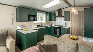 A compact kitchen with a microwave, stove, and sink, a dining area with a table and chairs, and a sofa. - 1 bedroom accommodation in Padstow (Padstow)
