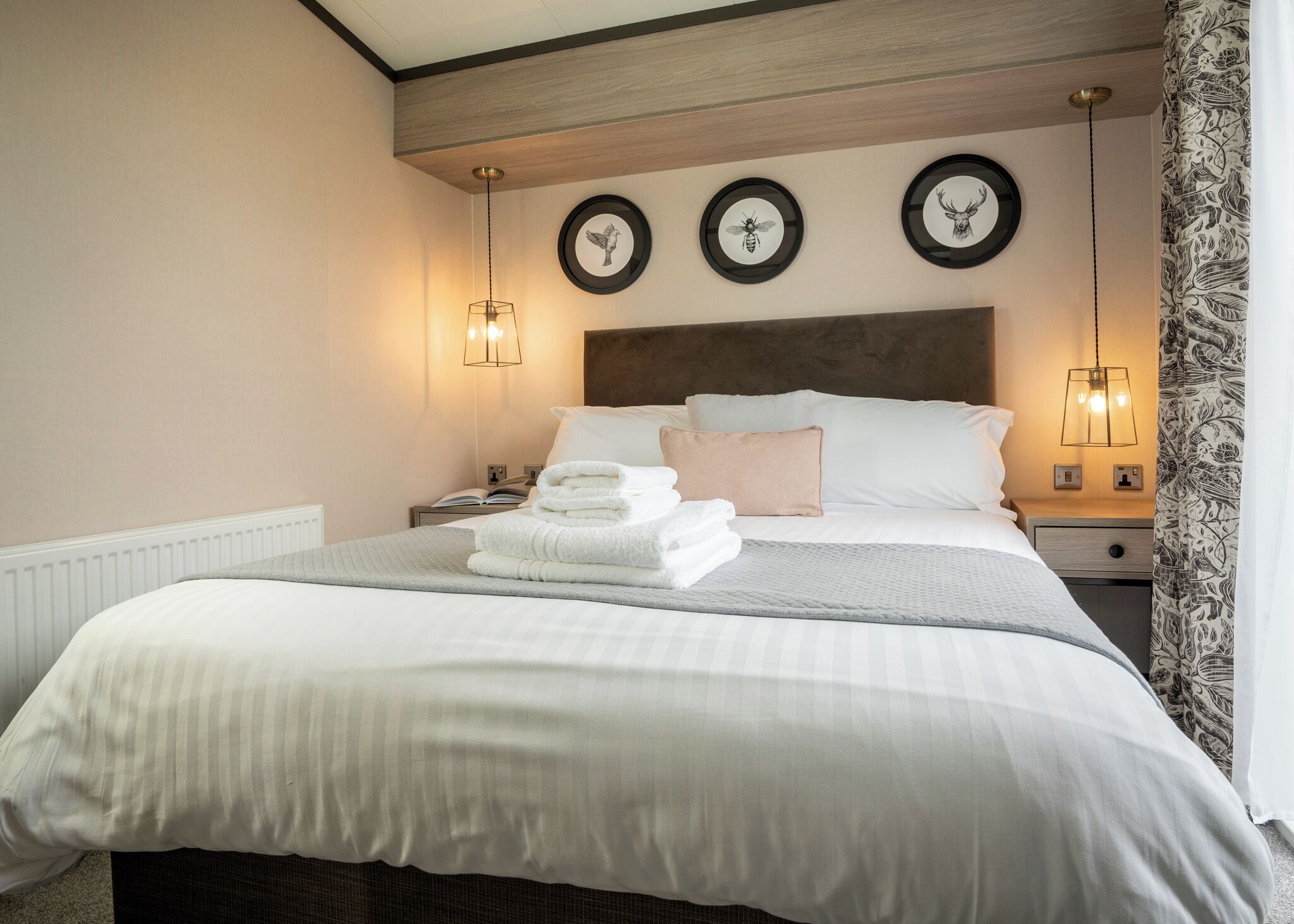 A neatly made bed with pillows and folded towels, a wooden headboard, and wall-mounted light fixtures.