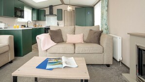 A living room with a sofa, a coffee table with magazines, a kitchen area with green cabinets, and a fireplace. - 1 bedroom accommodation in Padstow (Padstow)