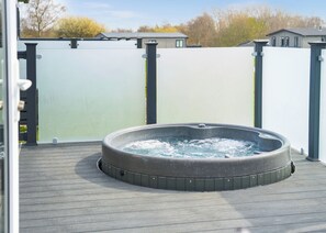 Un bain à remous sur une terrasse en bois, avec une clôture blanche et des maisons en arrière-plan.